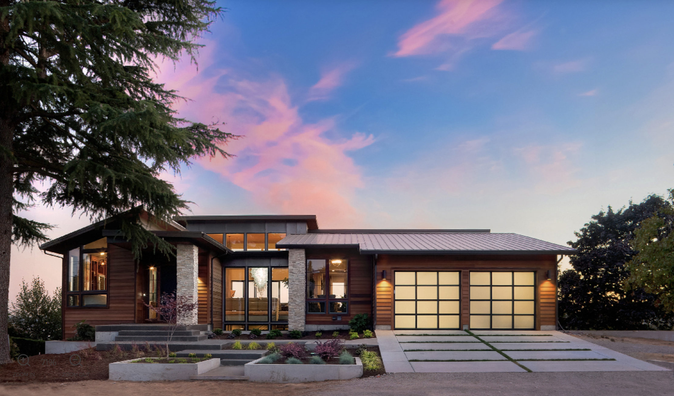 The front of a house at dusk, with the interior lights on and the driveway lit